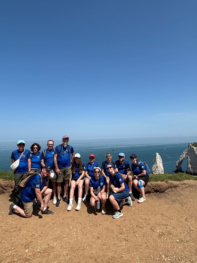 Les bénévoles de l'édition 2026, tous en t-shirt bleu, réunis au sommet des falaises d'Étretat, l'Aiguille en fond