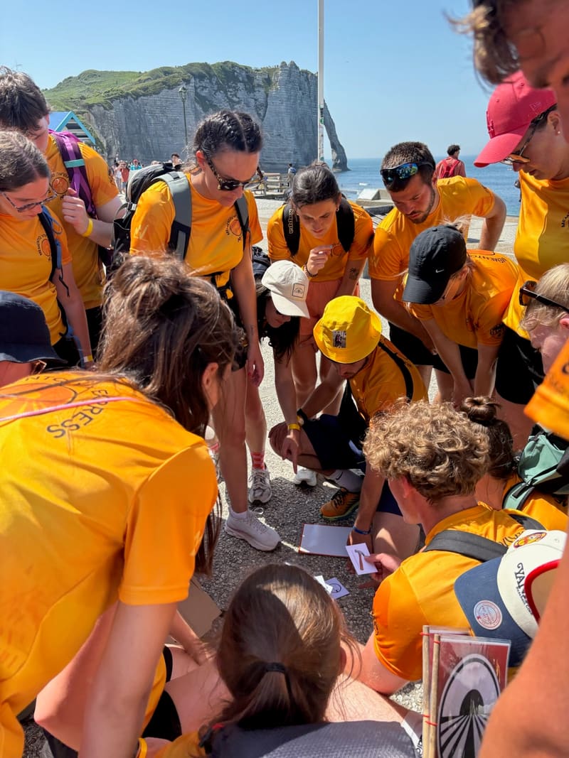 Les participants accroupis autour des cartes d'une épreuve, au pied des falaises d'Étretat