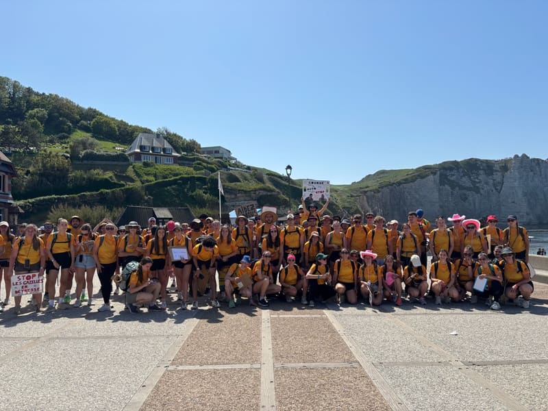 Le peloton sur l'esplanade d'Étretat, pancartes « Course auto-stop » levées